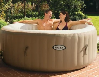 Мъж и жена се къпят в бежово надуваемо джакузи Intex PureSpa на тераса с червени плочки в градина