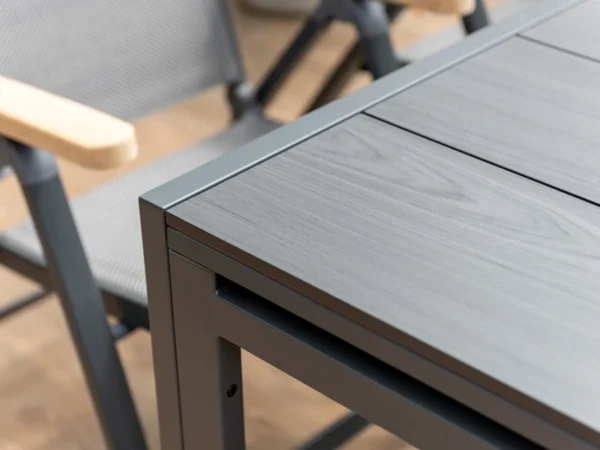 Ecke der Platte des Tisches Essence neben einem klappbaren Sessel mit Teak-Armlehnen