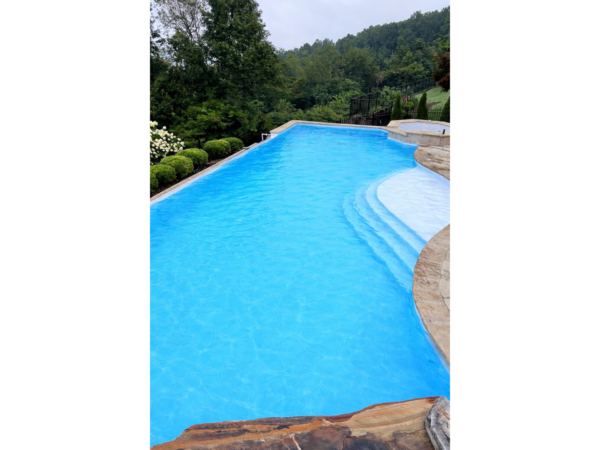 Piscină cu apă albastru deschis și liner armat Cefil Victoria Bianco printre păduri