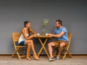 Două persoane beau cafea la măsuța din tec cu scaunele Ambra