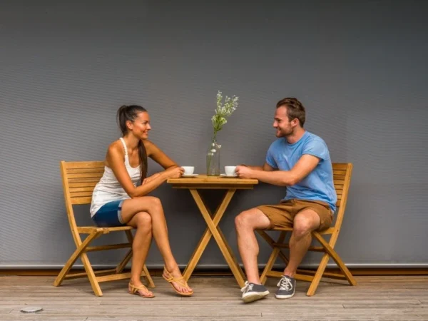 Două persoane beau cafea la măsuța din tec cu scaunele Ambra