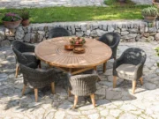 Masă rotundă din tec Colosseum cu fotolii împletite închise la culoare pe o terasă de piatră