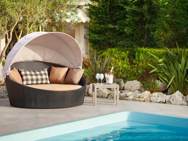 Градинска лежалка Kayu со настрешница и перници до базен, меѓу зеленило