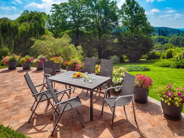 Alegria armchairs around a dark table on a terrace with flowers and a garden