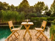 Balkontisch Ambra aus Teak mit einer Flasche und zwei Weingläsern auf einer Holzplattform am Wasser
