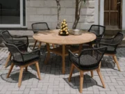 Colosseum round teak table with black Olivia armchairs in front of a stone wall