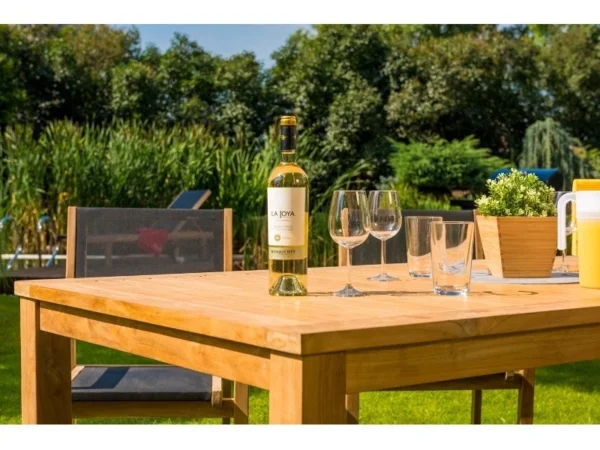 Platte des Tisches Vegas aus Teak mit Weinflasche und Gläsern vor dem Garten