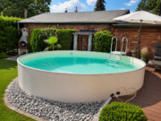 Halb eingelassener runder Pool MTH Atlantic Round mit weißer Wand und sandfarbener Auskleidung neben einem Gartenhaus