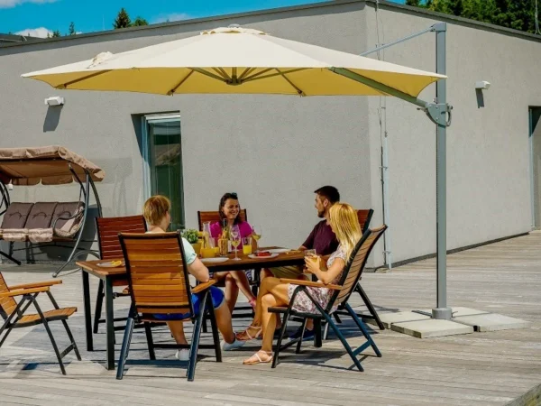 Φίλοι σε τραπέζι κάτω από ομπρέλα κήπου Borneo σε ξύλινη βεράντα