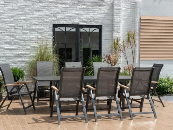Ausgezogener Tisch Essence mit klappbaren Sesseln auf einer Terrasse vor einer weißen Backsteinwand