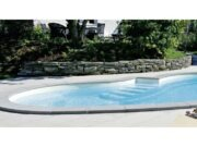 Toro XL coping stone from Carobbio around a pool with Roman stairs in a garden with a stone retaining wall